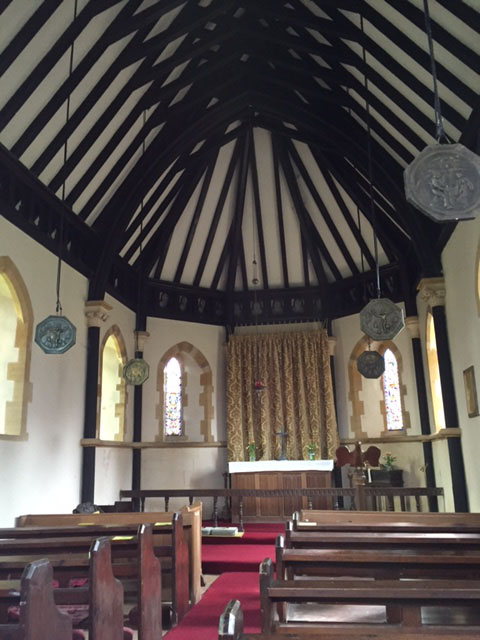 interior of Greenham church facing altar with ceiling beams and large hanging discs